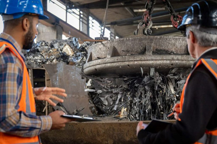 Two men stand before a large metal machine, discussing the magnate recycling processes in Dallas.