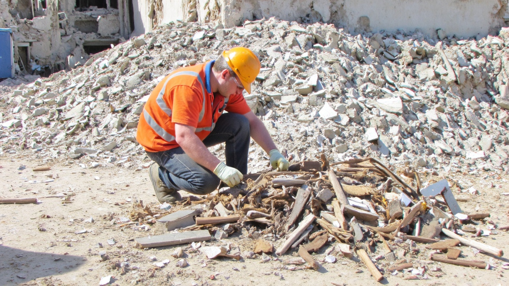 Construction Worker Sorting Recyclables Construction worker sorting recyclable materials from a demolished building, amidst organized piles of metal, wood, and concrete.