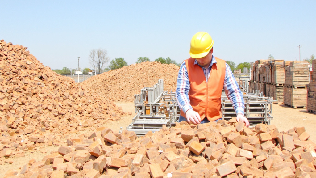 Sorting Recycled Materials at Construction Site Construction worker sorting recycled materials at a building site, with piles of sorted bricks, metal, and wood in the background