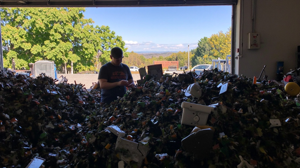 Recycling Facility Worker Sorting Components Worker sorting chiller components in a recycling facility with green trees and clear sky visible through the window.