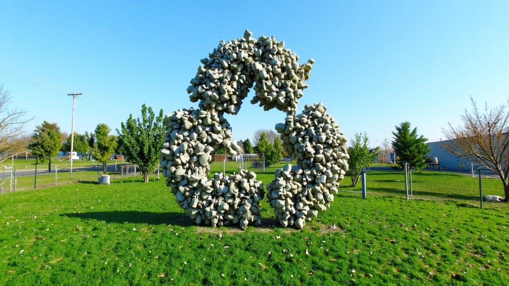 Lush Green Landscape with Recycling Symbol Lush green landscape with a recycling symbol made of concrete and metal pieces against a clear sky background